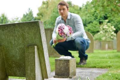 Man at cemetery with flowers grieving death of loved one in mourning