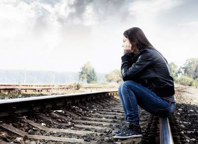 Depressed teenage girl sitting on train tracks staring into space sad